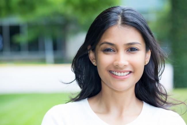 Closeup portrait of confident smiling happy pretty young woman in white shirt, isolated background of blurred trees. 
