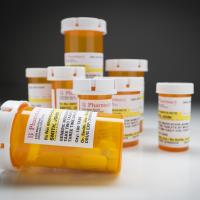 Variety of Non-Proprietary Medicine Bottles on Reflective Surface and Grey Background.