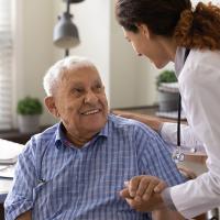 Nurse holding hand of smiling mature patient at meeting in hospital